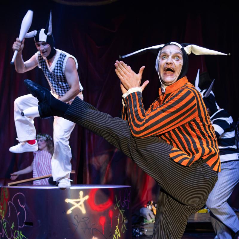 Sara P. Borgström Jyklare med svartvit mössa och rödsvart tröja kastar upp sitt ben i luften. I bakgrunden syns någon jonglera