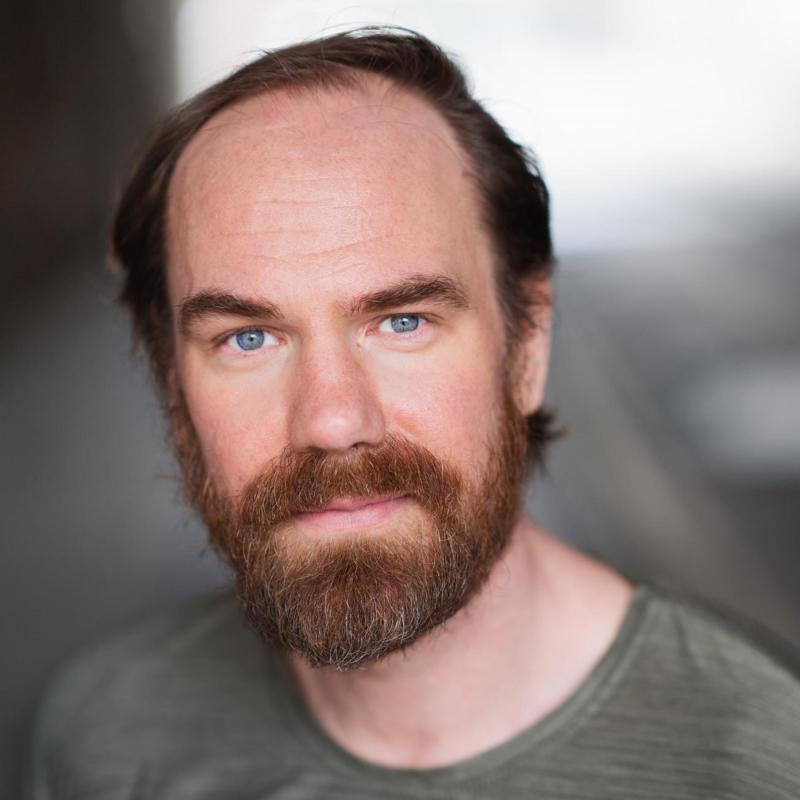 Porträttbild, person med rödlätthår och skägg tittar in i kameran