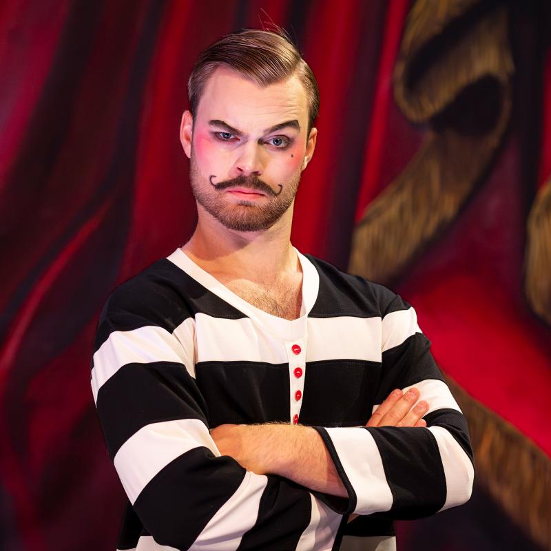 Person med vit och svartrandig tröja tittar strängt in i kameran. Vitmålat ansikte med röda kinder och påklistrad mustasch