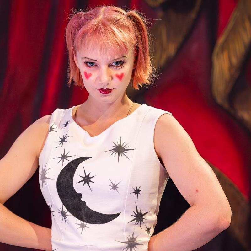 Person poserar med vitsminkat ansikte, röda hjärtan på kinderna och ett vitt linne