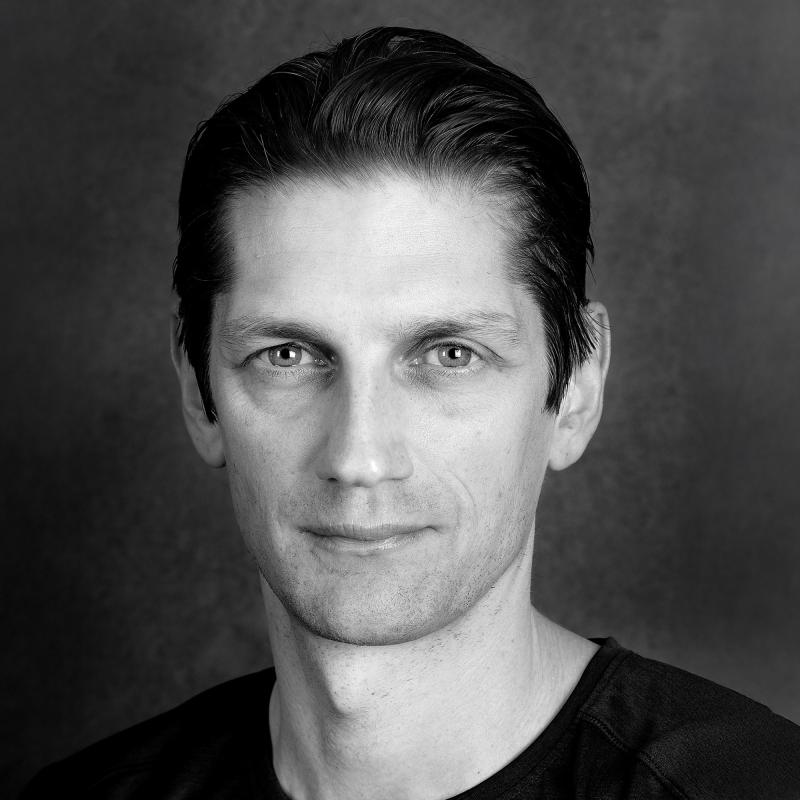 Porträttbild svartvit. Person med bakslickat hår och svart tshirt