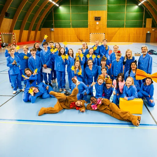 barn och vuxna iklädda blå pyjamasar, hållandes i gula stjärnor står i en sporthall. Två bär björnkostymer