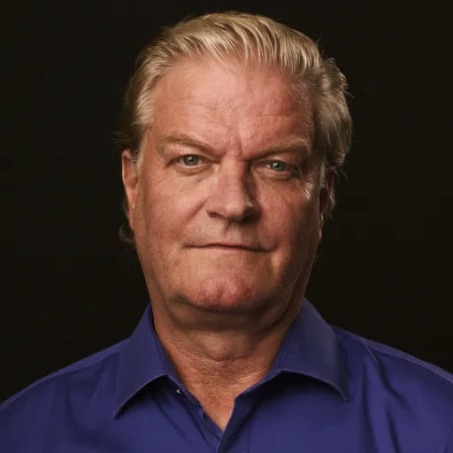 Porträttbild, äldre person med kort blont hår. Skjorta i kobolt blå syns sticka upp. 