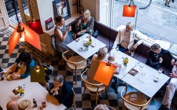 cafémiljö högt i tak, färgglada lampor, småbord med människor som äter och dricker