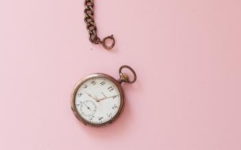 gammeldags klocka med kedja mot rosa bakgrund