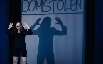 Skådespelaren står med upphöjda händer som syns som en större skugga i fonden.