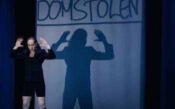 Skådespelaren står med upphöjda händer som syns som en större skugga i fonden.