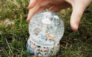 En barnhand tar tag om en snöglob som står på en gräsmatta