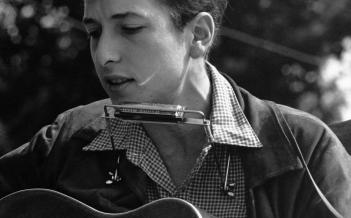 En ung Bob Dylan med akustisk gitarr och munspel 