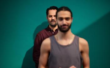 Två män står bakom varandra. Han längst bak syns skarpast.