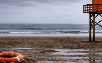 Bild på öde strand med en livboj och badvaktstorn