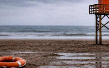 Bild på öde strand med en livboj och badvaktstorn
